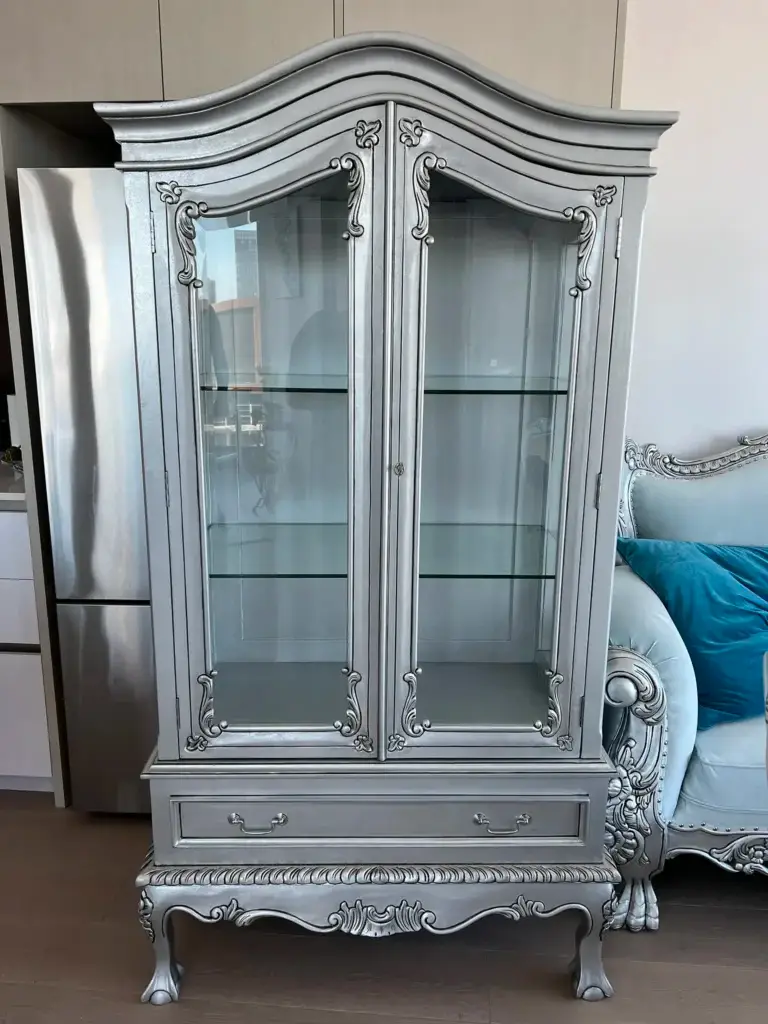 This is an image of a French Provincial glass display cabinet in antique silver leaf with bevelled glass doors and shelving, handcrafted by The Antique Reproduction Shop