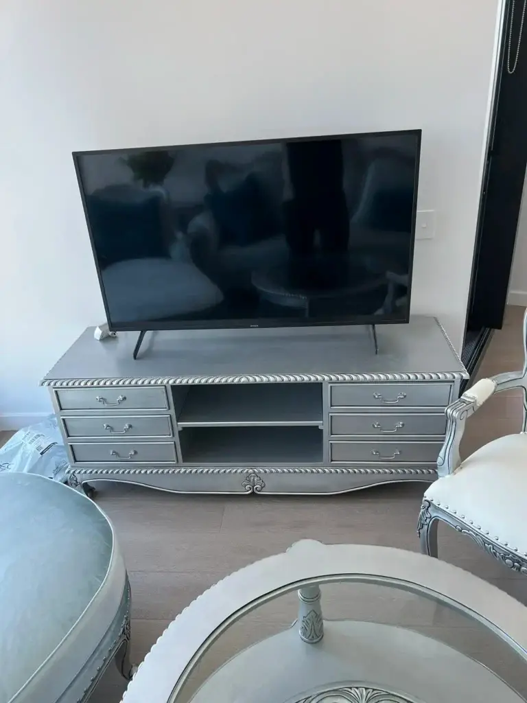This is an image of a carved round French Provincial coffee table with a glass insert and antique silver finish, designed by The Antique Reproduction Shop