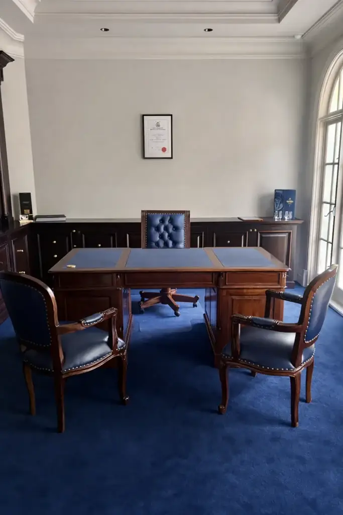 This is an image of a handcrafted mahogany office chair upholstered in genuine navy leather with button tufting and brass stud detailing from The Antique Reproduction Shop